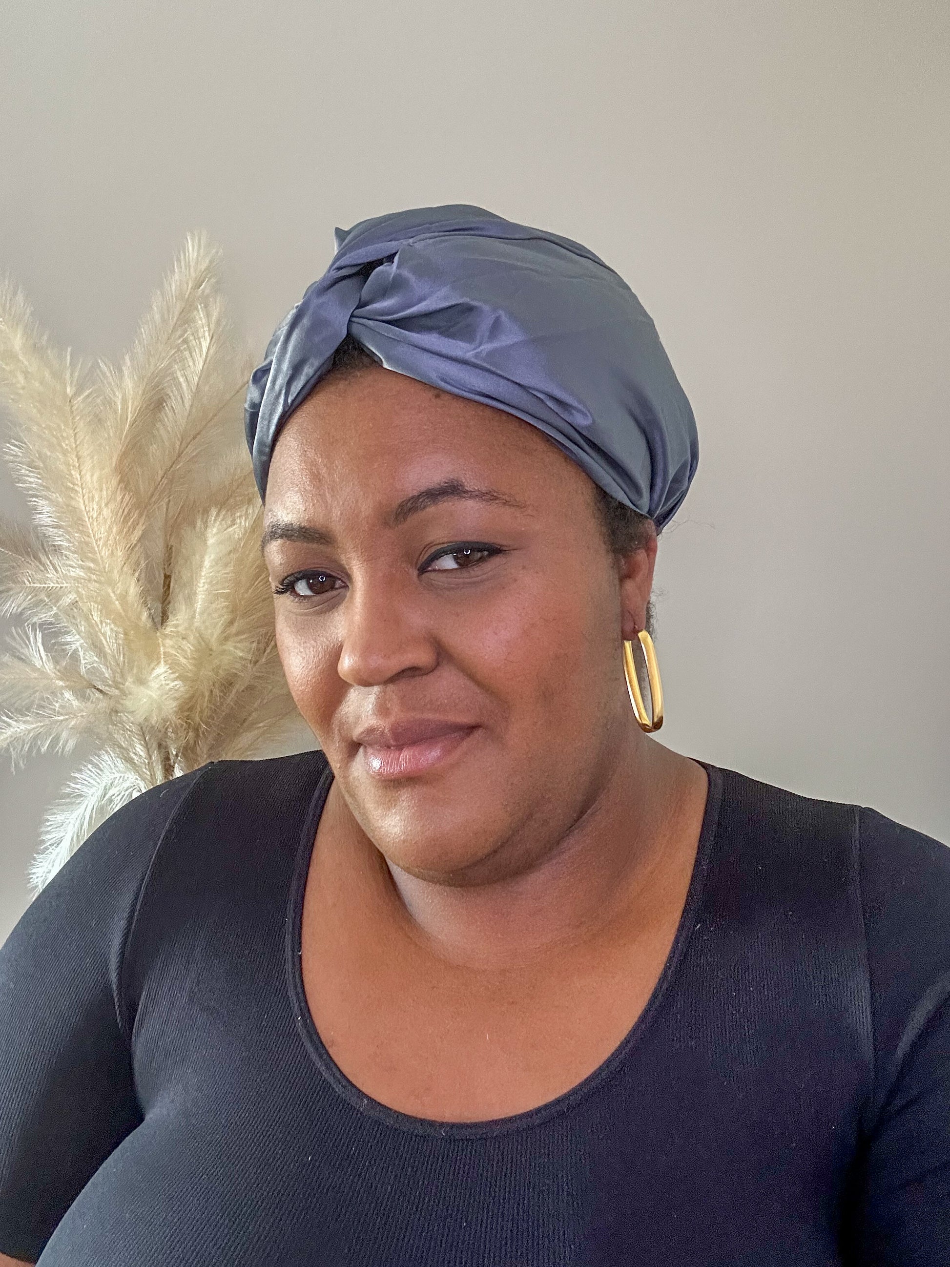 silk bonnet with twist detail at front - on black model with pampas grass in background charcoal grey