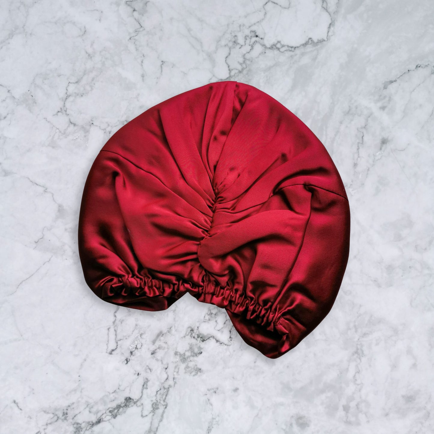 Elastic back of red silk satin hair bonnet on a marble surface