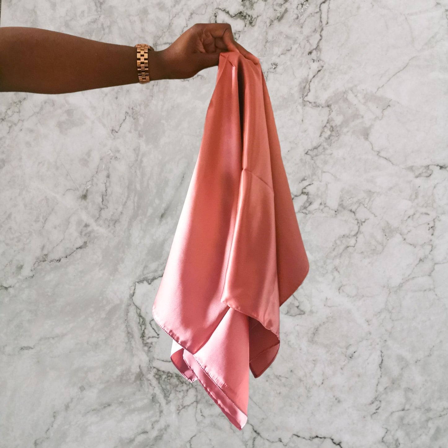 Mulberry silk large square scarf in copper rose colour held by model in front of marble background