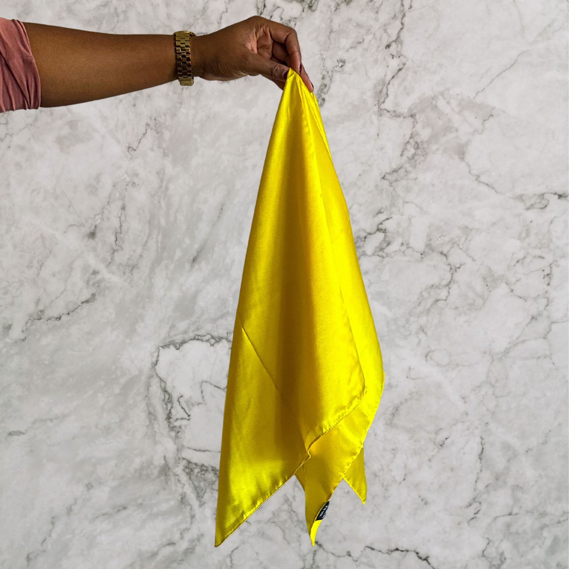 Hand holding a yellow silk hair scarf against a marble background