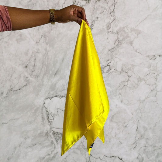 Hand holding a yellow silk hair scarf against a marble background
