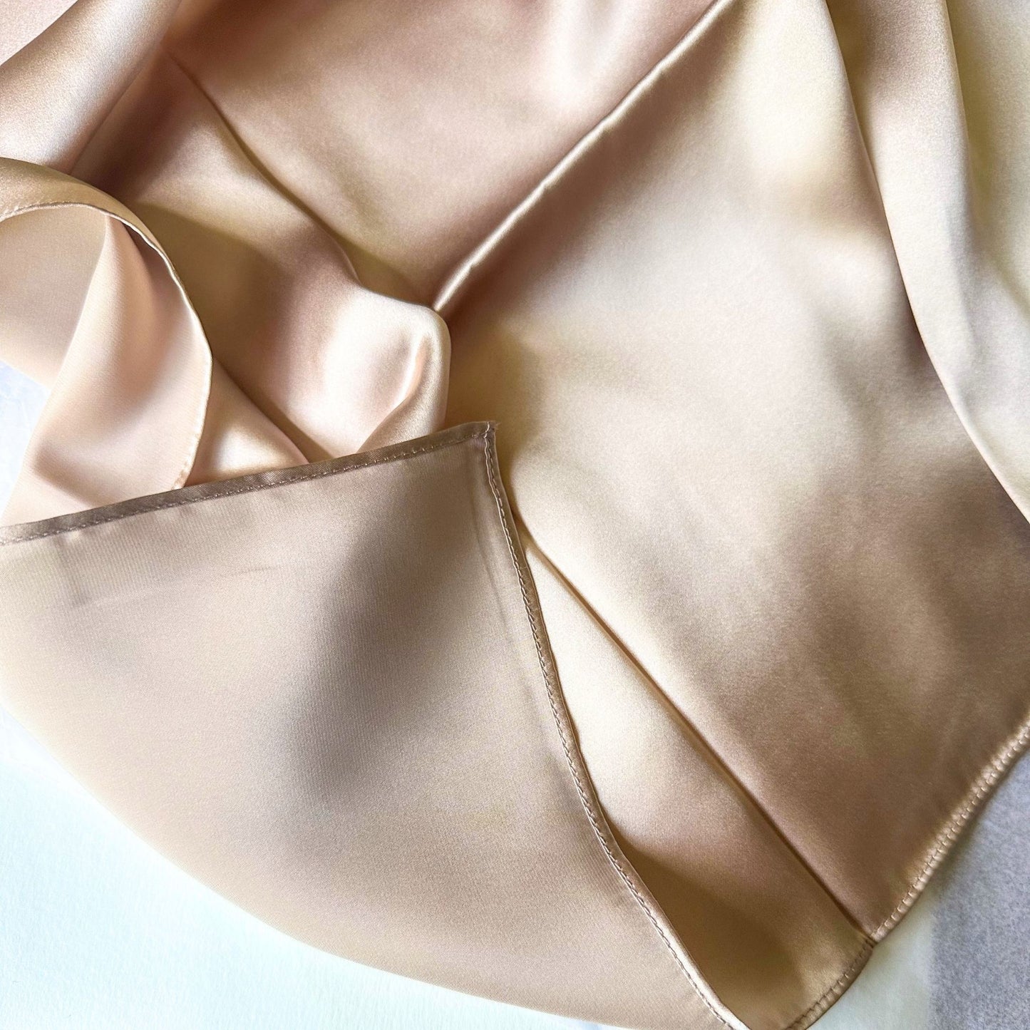A close-up of mulberry silk hair scarf for sleeping in a soft champagne beige color, showing its smooth texture and subtle sheen.