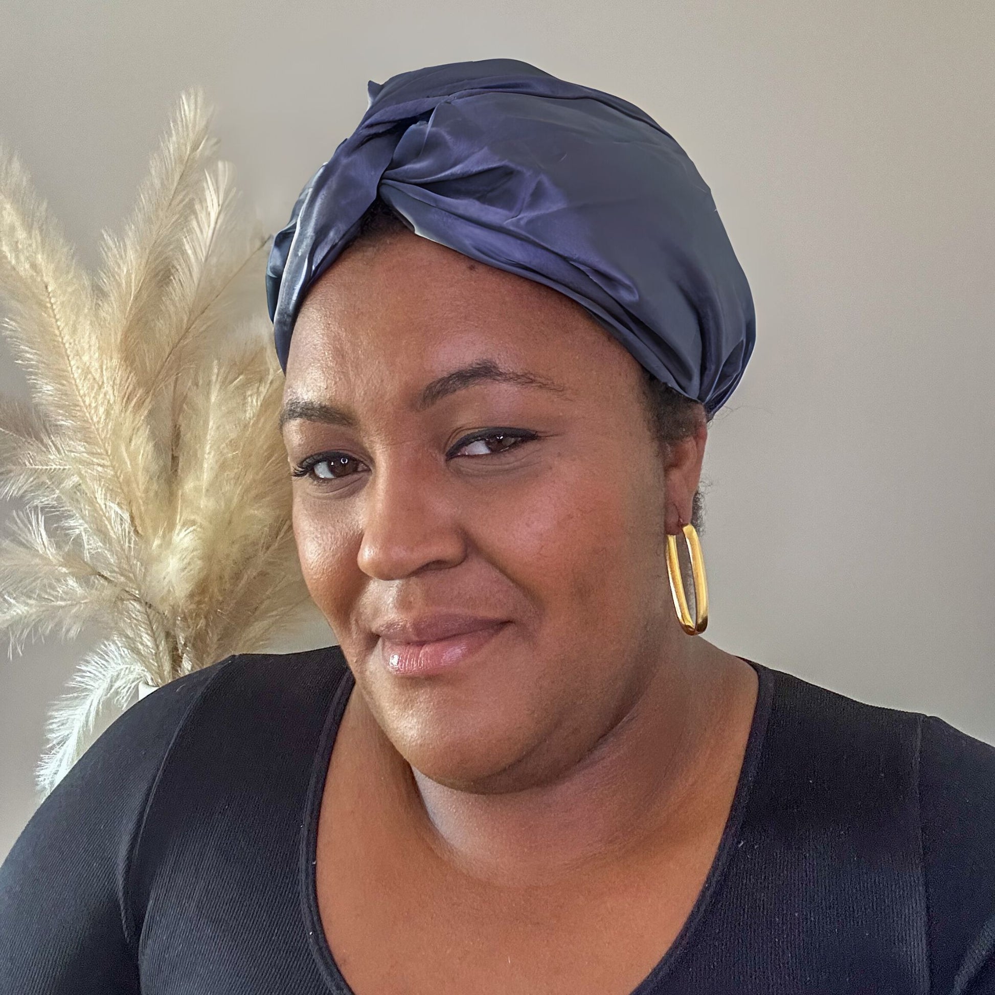silk bonnet with twist detail at front - on black model with pampas grass in background dark charcoal grey