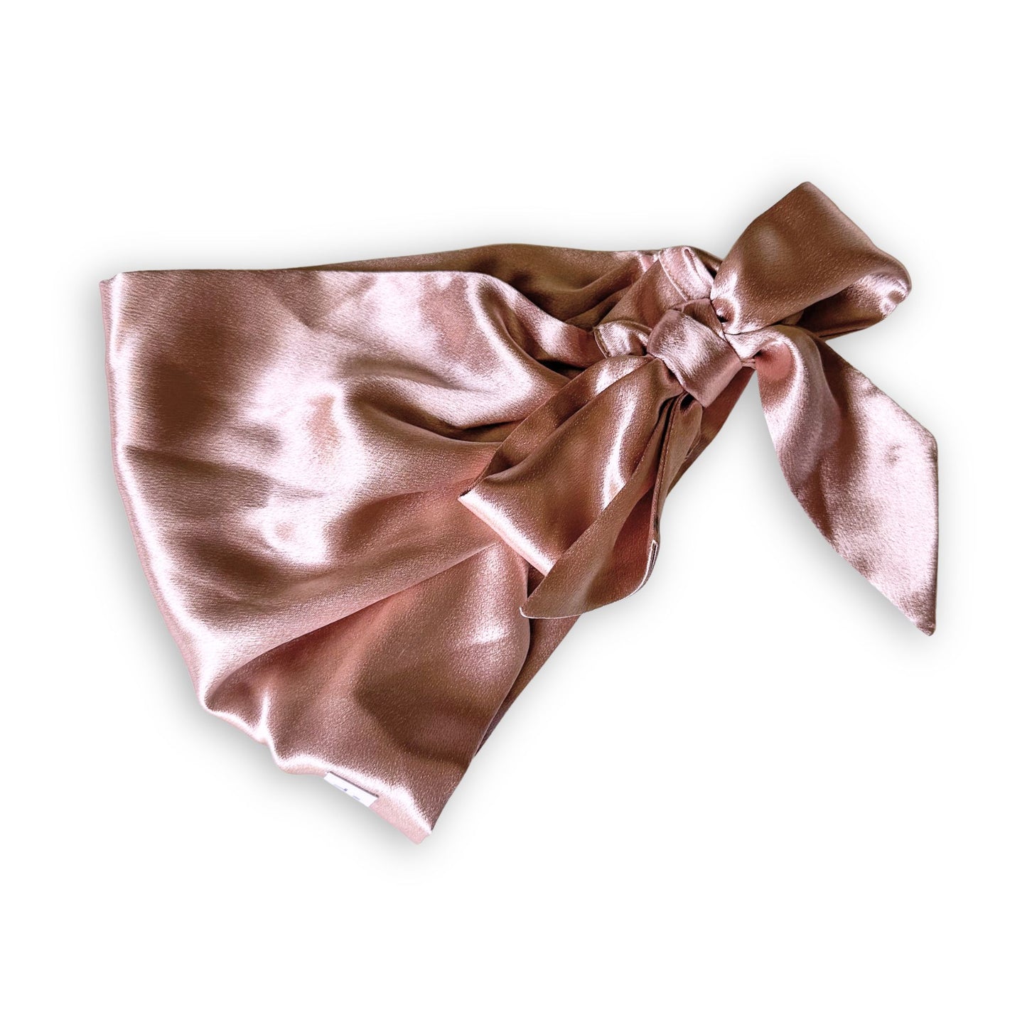 a beige glossy satin hair scarf tied in a bow laid flat on a plain white background